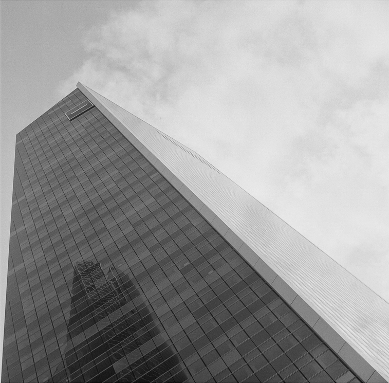 Tall modern skyscraper with reflective glass windows, resembling a tour de verre, photographed from a low angle against a cloudy sky, creating a dramatic perspective.