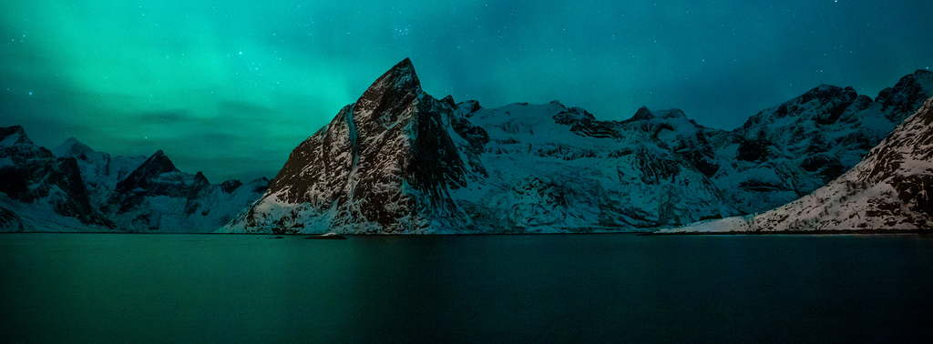 Aurore boréale / Hamnoy / Lofoten / Norvège An ethereal night sky illuminated by the green glow of the aurora borealis over snow-capped mountains reflected in the still, dark waters of a fjord near Hamnoy. Rugged peaks reach skyward, creating a serene and mystical landscape in Lofoten.